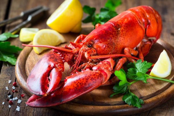 A cooked lobster decoratively placed on a plate with lemon wedges and parsley.